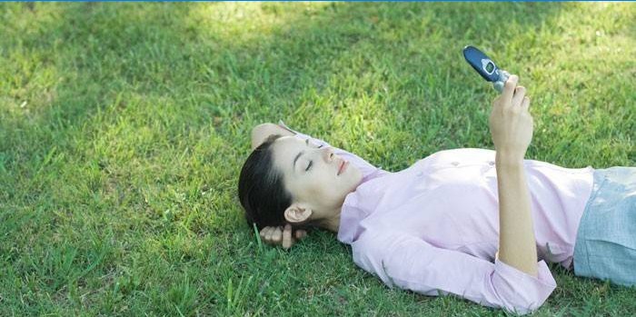 La jeune fille se trouve sur l'herbe avec un téléphone
