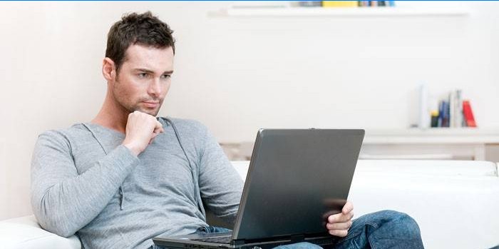 Un homme est assis sur un canapé avec un ordinateur portable