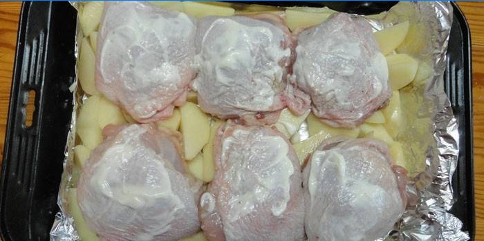 Cuisses de poulet sur un oreiller de pommes de terre avant cuisson sur une plaque à pâtisserie