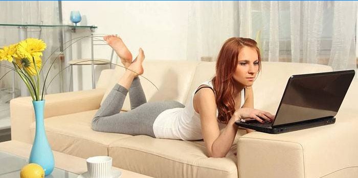 La jeune fille se trouve sur un canapé avec un ordinateur portable