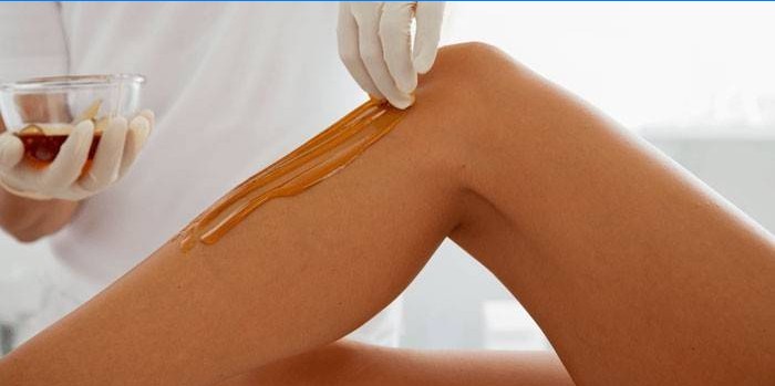 L'esthéticienne applique une pâte pour l'épilation sur la peau des jambes.